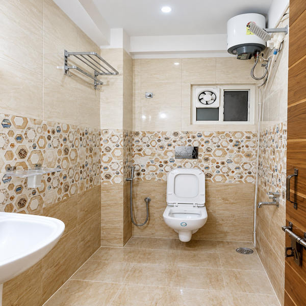 Modern bathroom, contemporary bathroom, beige bathroom, tiled bathroom, bathroom interior, Indian bathroom design, residential bathroom, wall tiles, patterned wall tiles, geometric tiles, hexagon tiles, beige marble tiles, floor tiles, ceramic tiles, porcelain tiles, toilet design, western toilet, wall mounted toilet, bathroom ventilation, exhaust fan, bathroom window, water heater, geyser, shower area, handheld shower, bathroom faucet, wash basin, pedestal sink, bathroom fixtures, sanitary ware, towel rack, stainless steel rack, bathroom storage, utility bathroom, compact bathroom, spacious bathroom, clean bathroom, neutral bathroom, warm beige tones, marble effect tiles, decorative tiles, accent tile wall, bathroom renovation, modern sanitaryware, bathroom decor, functional bathroom, minimalist bathroom, Indian home bathroom, apartment bathroom, house bathroom, tiled walls, tiled floor, plumbing fixtures, wall mounted accessories, ventilation window, bathroom lighting, ceiling light, bright bathroom, hygienic bathroom, practical design, contemporary sanitaryware, toilet room, bathroom layout, residential interior, home improvement, bathroom remodeling, modern home design, beige interior, stone texture, geometric pattern, patterned backsplash, floor drain, bathroom door, wooden bathroom door, utility fittings, water heater installation, exhaust ventilation, compact washroom, modern washroom, clean tile design, neutral palette, simple bathroom, elegant bathroom, functional interior, durable tiles, easy maintenance bathroom, bathroom inspiration, interior design ideas, Indian interior decor, home renovation ideas, contemporary home, modern house, bathroom styling, bathroom fixtures design, tiled washroom, residential washroom, premium bathroom design, practical home interiors, bathroom photography, modern toilet room.